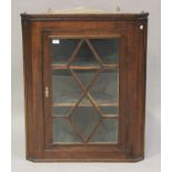 A George III oak hanging corner display cabinet, the astragal glazed door revealing a green