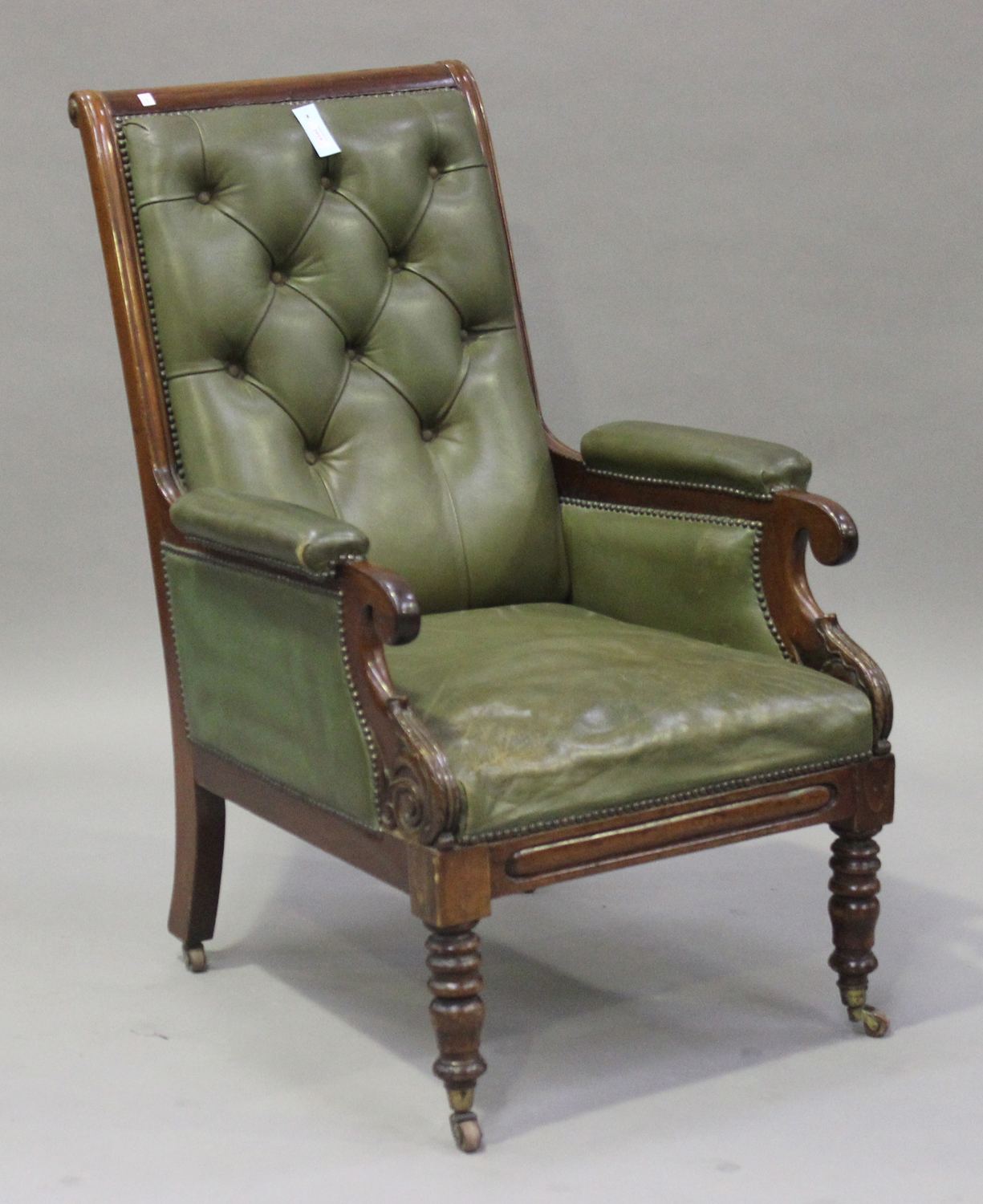 An early Victorian mahogany library armchair, upholstered in green buttoned leather, raised on