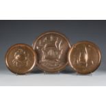 A group of three Arts and Crafts Newlyn copper circular dishes, one decorated in relief with a crab,