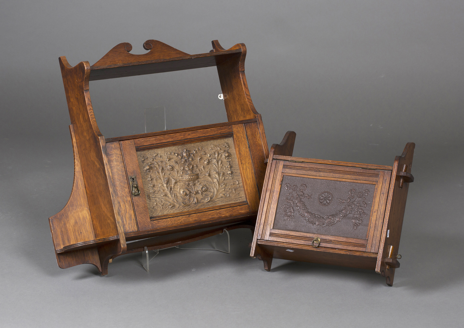 An Edwardian Arts and Crafts oak hanging wall shelf, the cabinet door inset with a relief foliate