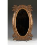 An early 20th century Arts and Crafts oak oval wall mirror, the frame carved with poppy seedpods and