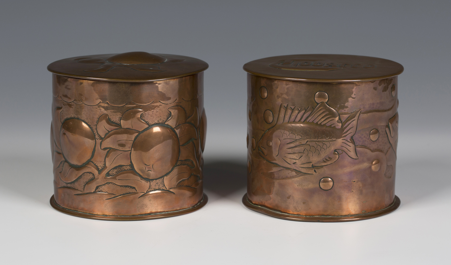 Two Arts and Crafts Newlyn copper jars and covers of cylindrical form, one decorated with overall