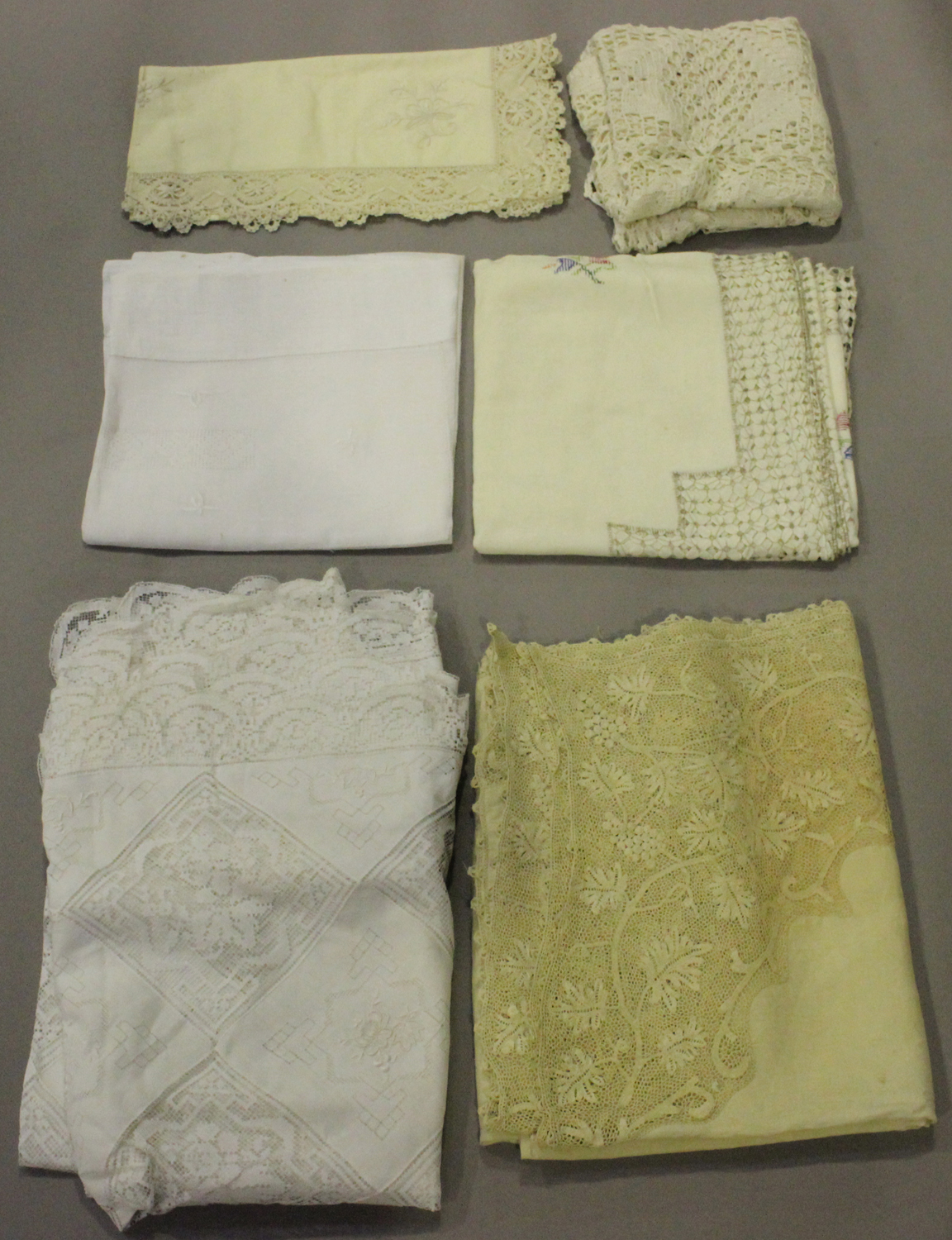 A small group of textiles, including an ivory-toned linen tablecloth with cellular lacework