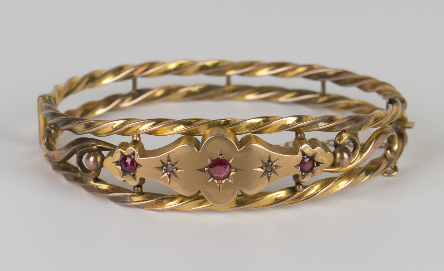 A 9ct gold, diamond and red gem set oval hinged bangle, decorated with ropetwist openwork sides,