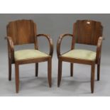 A pair of Art Deco French walnut elbow chairs with shaped panel backs and curved armrests, raised on