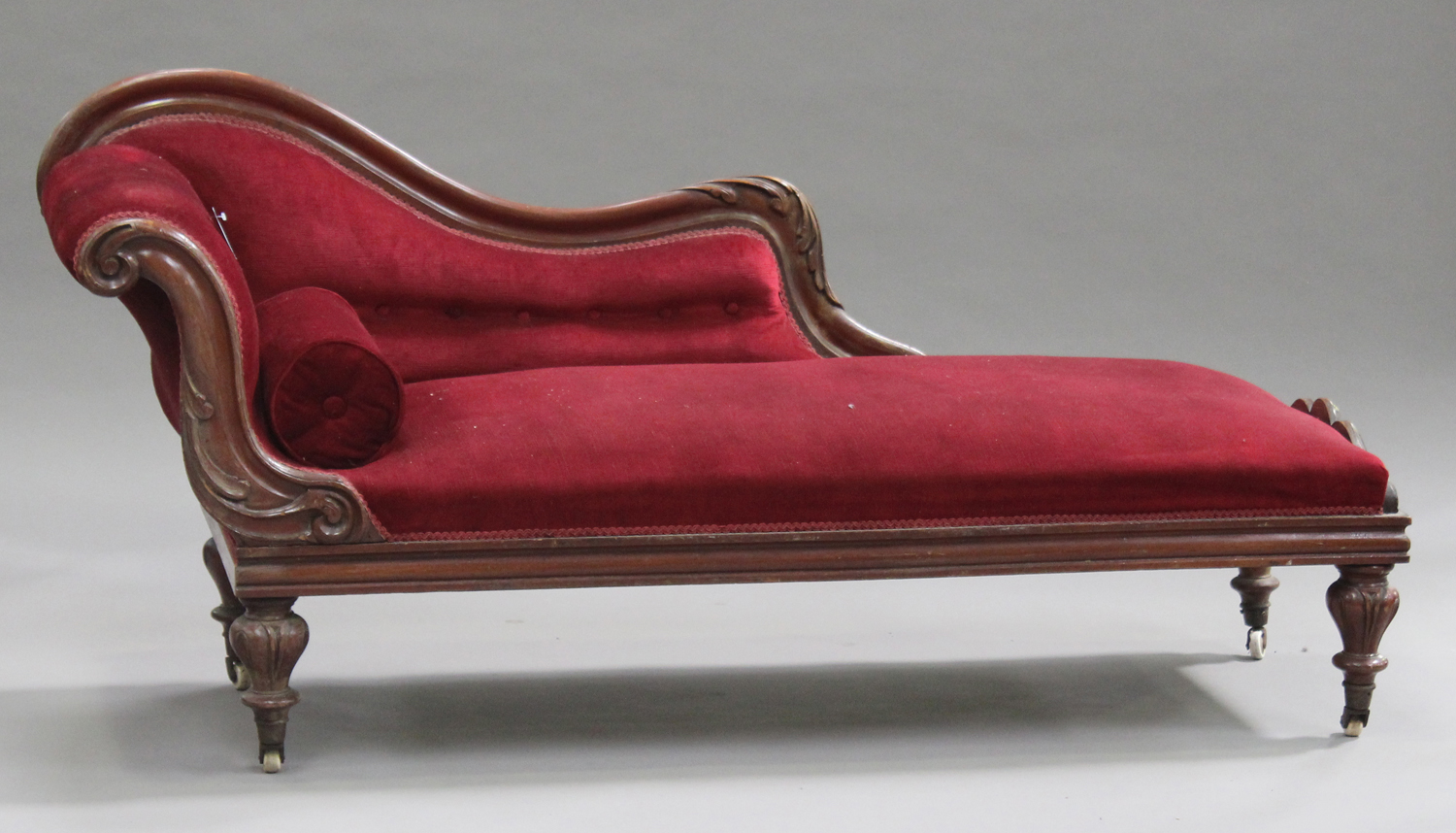 A Victorian mahogany framed chaise-longue with carved decoration, upholstered in red velour,