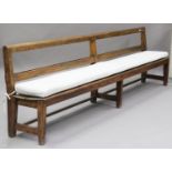 A late 19th/early 20th century pine framed long bench pew, the open rail back above a solid seat, on