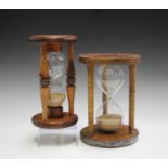 Two 20th century sand timer hourglasses, mounted within wooden frames, heights 24cm and 25cm.Buyer’s