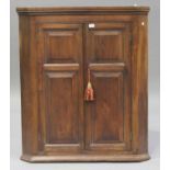 A George III elm hanging corner cabinet, fitted with a pair of fielded panel doors revealing