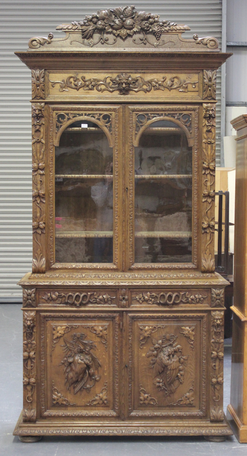 A mid-Victorian oak bookcase cabinet, profusely carved with floral scrolls and masks, the moulded