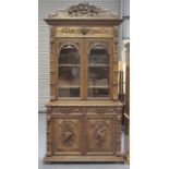 A mid-Victorian oak bookcase cabinet, profusely carved with floral scrolls and masks, the moulded