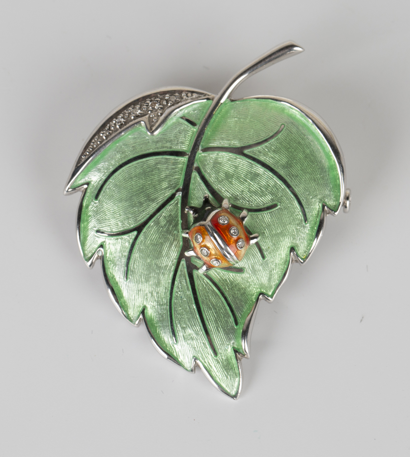 A silver, enamelled and diamond pendant brooch in the form of a ladybird perched on a leaf, length