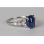 A platinum, cabochon sapphire and diamond ring, claw set with an oval cabochon sapphire between