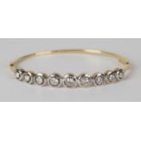 A gold and diamond oval hinged bangle, the front collet set with a row of nine circular cut diamonds