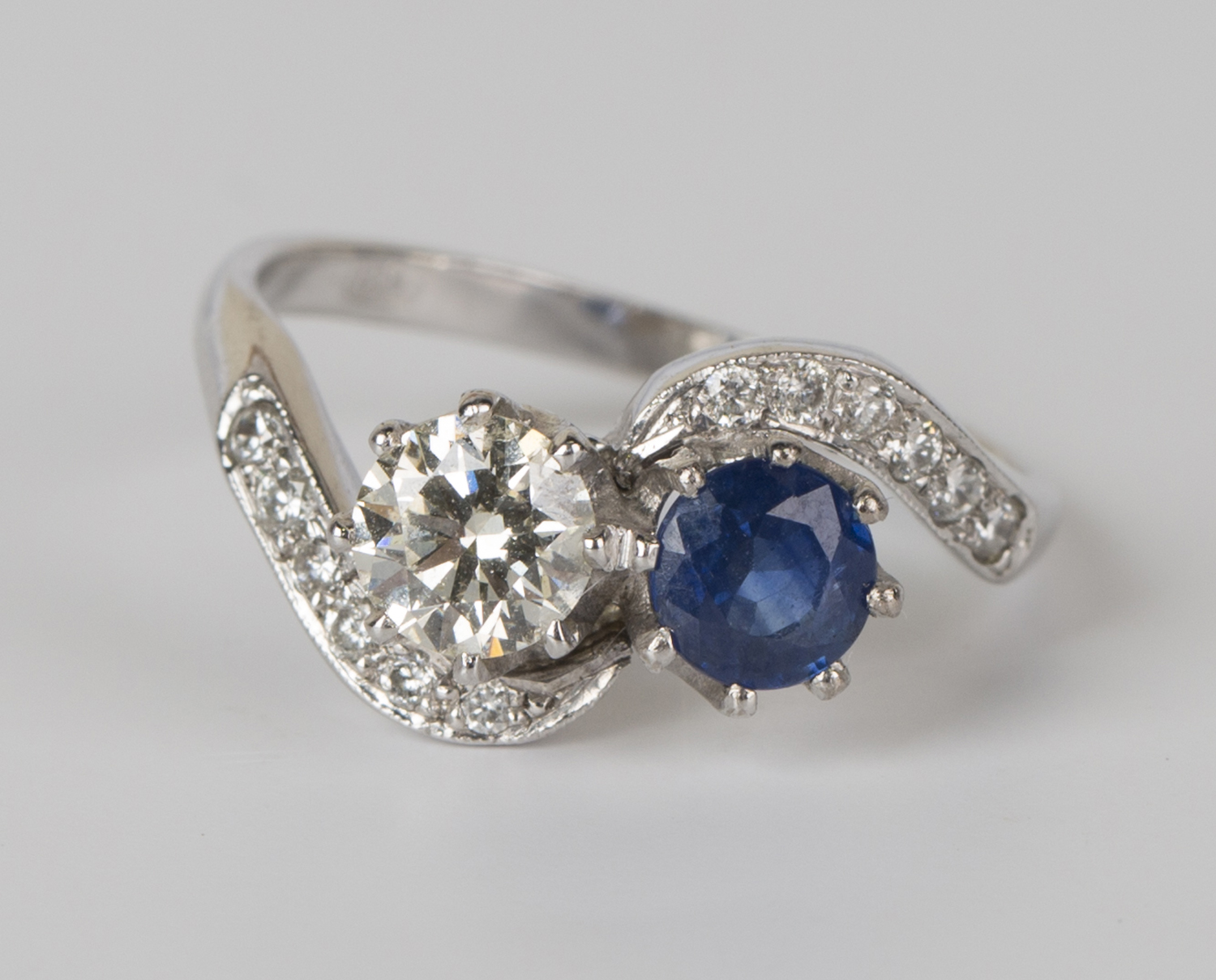 A white gold, diamond and sapphire crossover ring, claw set with the principal circular cut