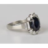 A white gold, sapphire and diamond cluster ring, claw set with an oval cut sapphire between