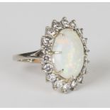 A white gold, opal and diamond ring, claw set with an oval opal within a surround of circular cut
