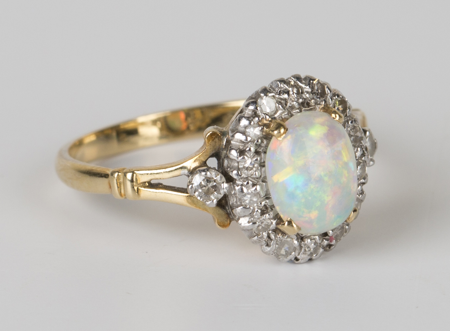A gold, platinum, opal and diamond oval cluster ring, claw set with an oval opal within a surround