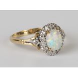 A gold, platinum, opal and diamond oval cluster ring, claw set with an oval opal within a surround