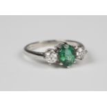 A platinum, emerald and diamond ring, claw set with an oval cut emerald between circular cut diamond
