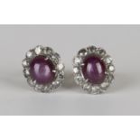A pair of white gold, star ruby and diamond cluster earrings, claw set with an oval cabochon star