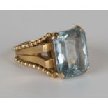 A gold ring, claw set with a cut cornered rectangular mixed cut aquamarine between beaded 'V' shaped