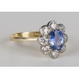 A gold, sapphire and diamond oval cluster ring, claw set with an oval cut sapphire within a surround