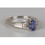 A white gold, blue gemstone and diamond ring, claw set with the oval cut blue gemstone between two