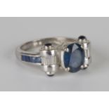 An 18ct white gold, sapphire and diamond ring, claw set with the principal oval cut sapphire between