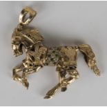 A 9ct gold, green and colourless gem set pendant, designed as an articulated horse, length 6cm.