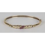 A 9ct gold, ruby and diamond oval hinged bangle, claw set with a row of three circular cut rubies