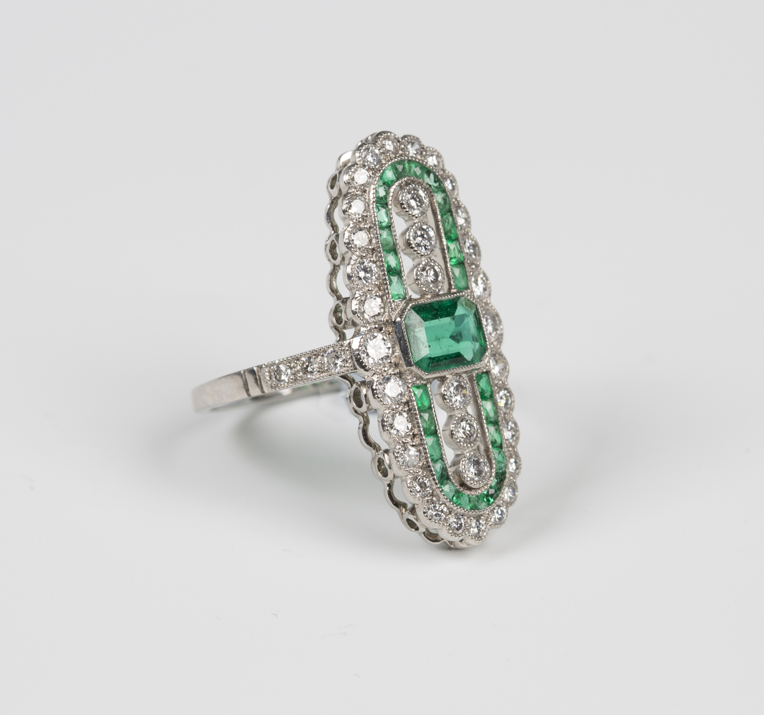 A platinum, emerald and diamond open panel shaped ring, mounted with a cut cornered rectangular