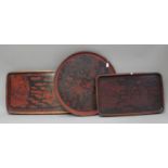Three Japanese black and dark red lacquered trays, early 20th century, comprising two rectangular,