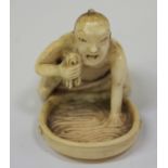 A Japanese carved ivory netsuke, Meiji period, modelled as a man kneeling over a shallow bowl of