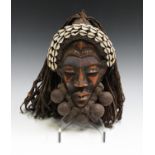 A Dan carved and stained wooden mask, Ivory Coast, with applied cowrie shells and woven string