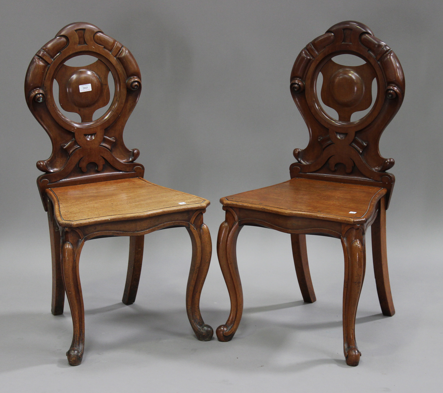 A pair of Victorian mahogany hall chairs with carved scroll decoration, the solid seats raised on