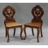 A pair of Victorian mahogany hall chairs with carved scroll decoration, the solid seats raised on