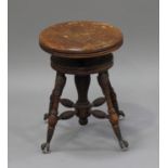 A late 19th century American walnut revolving piano stool, the ring turned legs terminating in