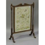 An early 20th century oak framed firescreen, inset with a floral needlework panel, on scroll feet,