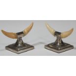 A pair of Edwardian silver and ivory mounted knife rests, designed as a pair of carved ivory '