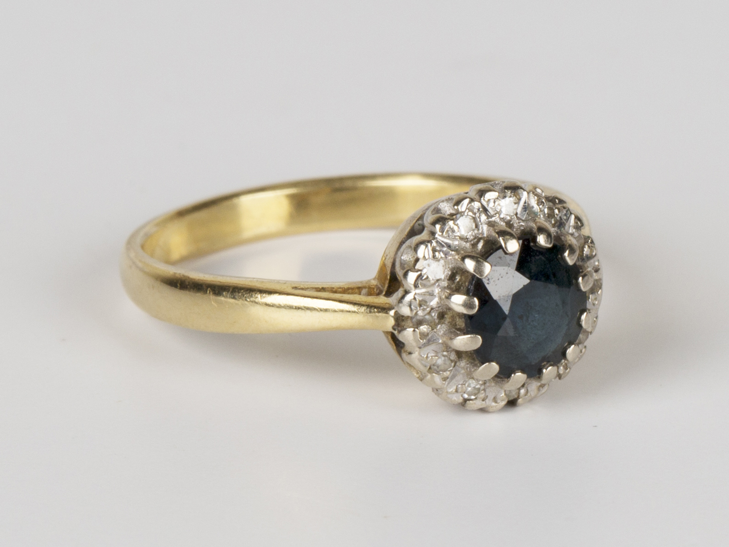 A gold, sapphire and diamond circular cluster ring, claw set with a circular cut sapphire within a