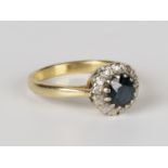 A gold, sapphire and diamond circular cluster ring, claw set with a circular cut sapphire within a