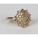 A 9ct gold and diamond cluster ring in a shaped circular design, mounted with circular cut champagne