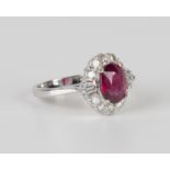 An 18ct white gold, ruby and diamond ring, claw set with an oval cut ruby within a surround of