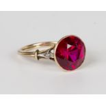 A gold ring, collet set with a circular cut synthetic ruby between rose cut diamond set shoulders,