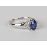 An 18ct white gold, sapphire and diamond ring, claw set with the oval cut sapphire between diamond