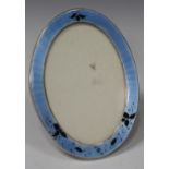 A George V silver, blue and black enamelled oval photograph frame, decorated with scattered leaves