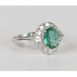 An 18ct white gold, emerald and diamond ring, claw set with an oval cut emerald within a surround of