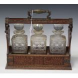 An Edwardian oak and plate mounted three-bottle tantalus, the three cut glass decanters held