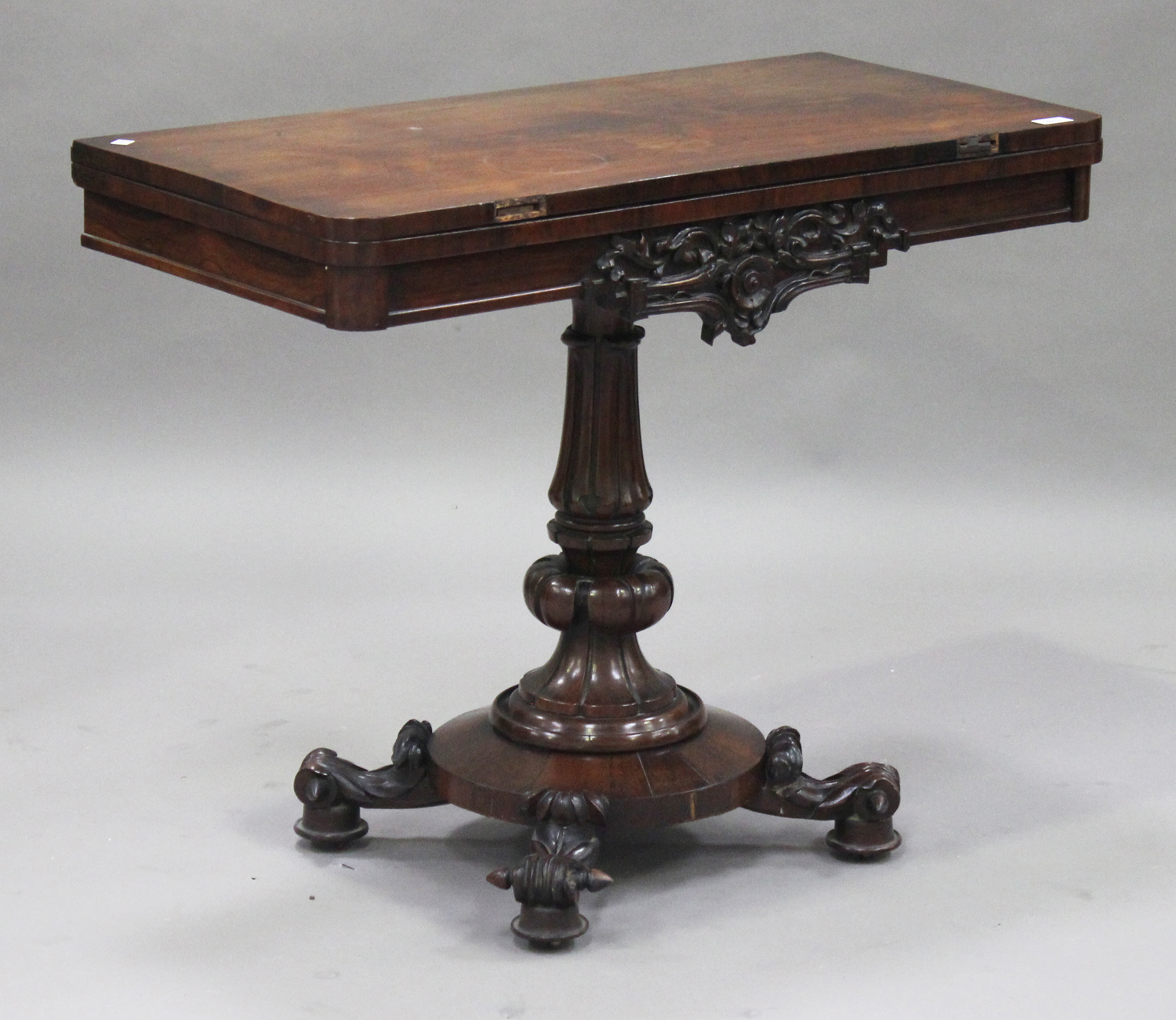 An early Victorian rosewood fold-over card table, raised on a turned and carved baluster column, the